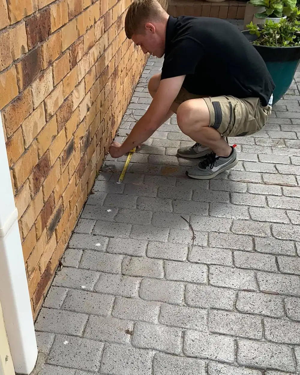 Ecology-Care technician measuring along the base of a brick wall during a termite inspection